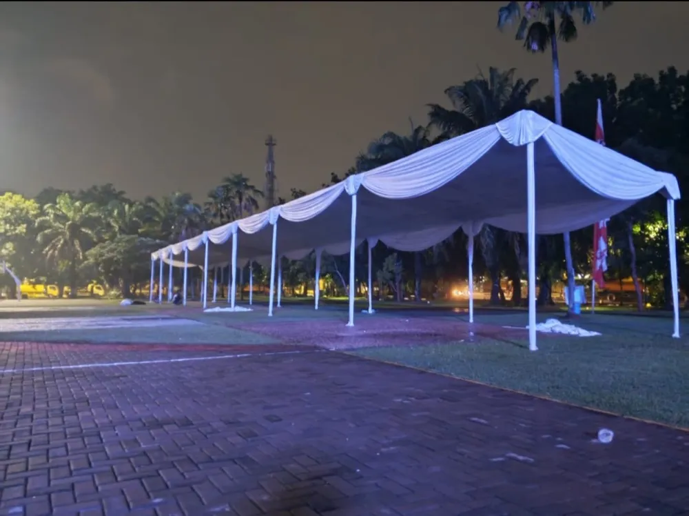 Deretan tenda dekor putih memanjang di taman pada malam hari